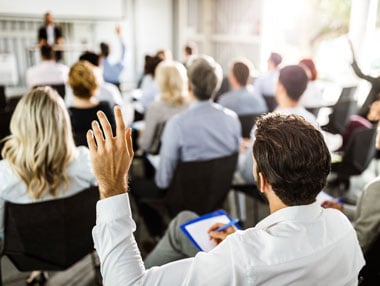 Man with hand up to ask a question at a conference